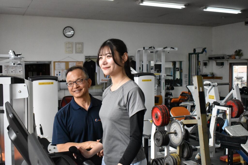 A trainer checking in with a member beside the treadmill at Orange Fitness, Kai City, Yamanashi